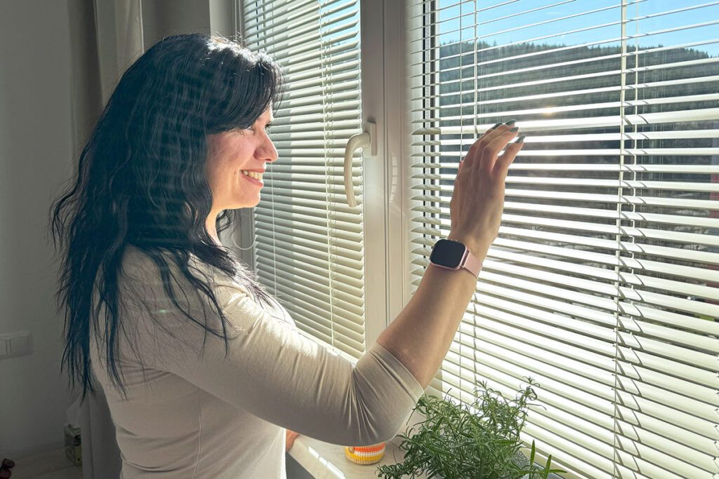 Žena se jemně dotýká bílé vnitřní žaluzie IDX od CLIMAXu