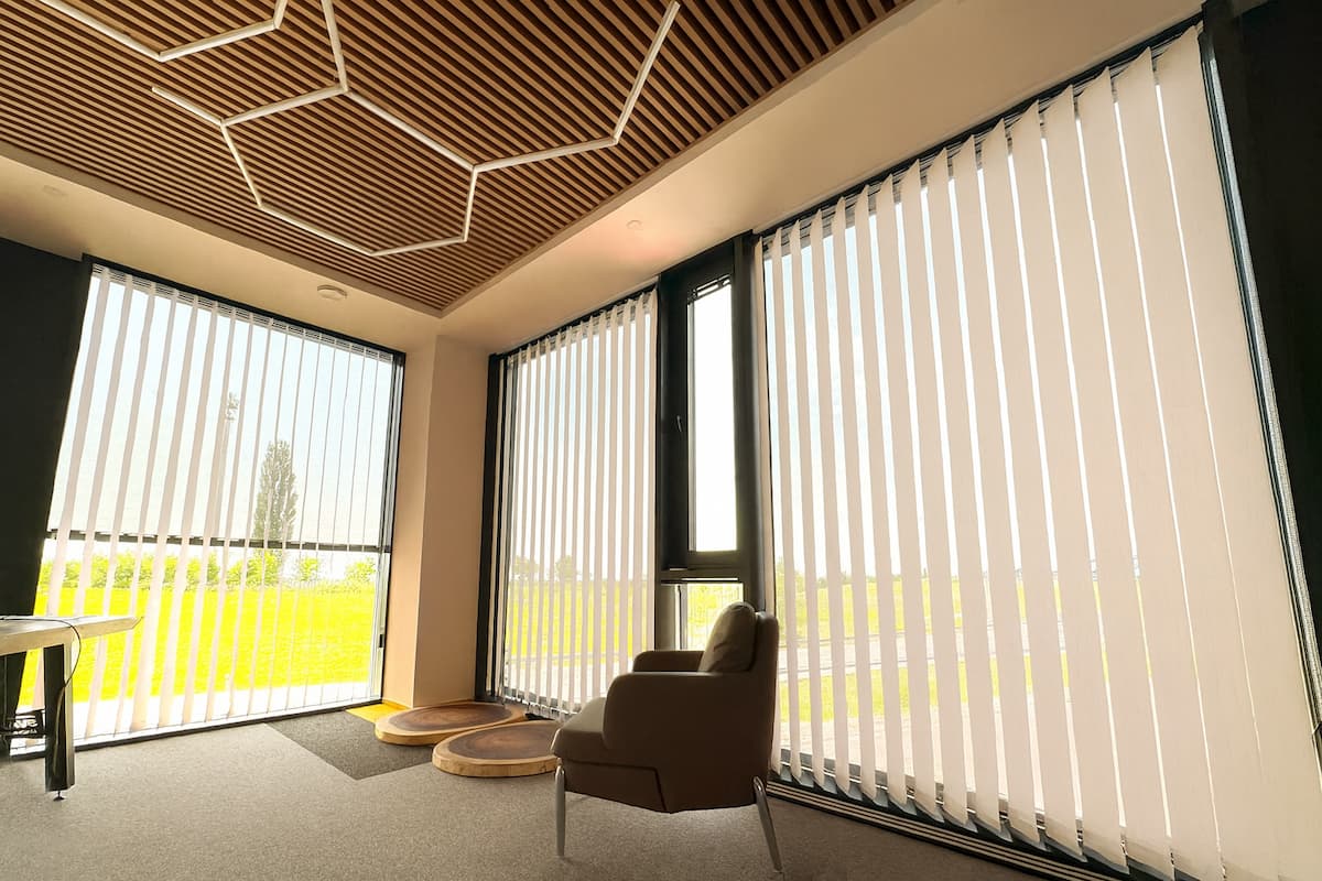 Interiér se svislými látkovými žaluziemi na okna, které propouštějí jemné denní světlo.