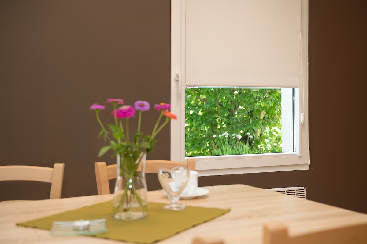 Interiér jídelny s látkovou roletou na okně a výhledem do zeleně.