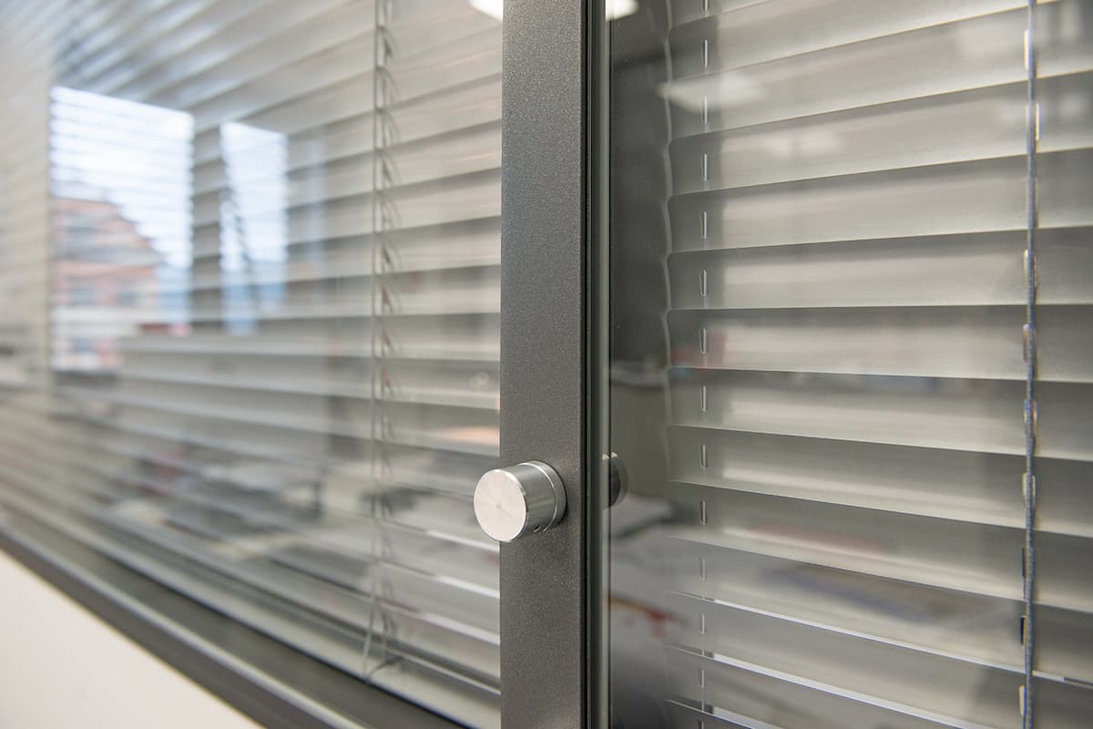 Detail meziskelní žaluzie s mechanickým ovládáním, kde je naklápění lamel pomocí kolečka integrováno do rámu okna.