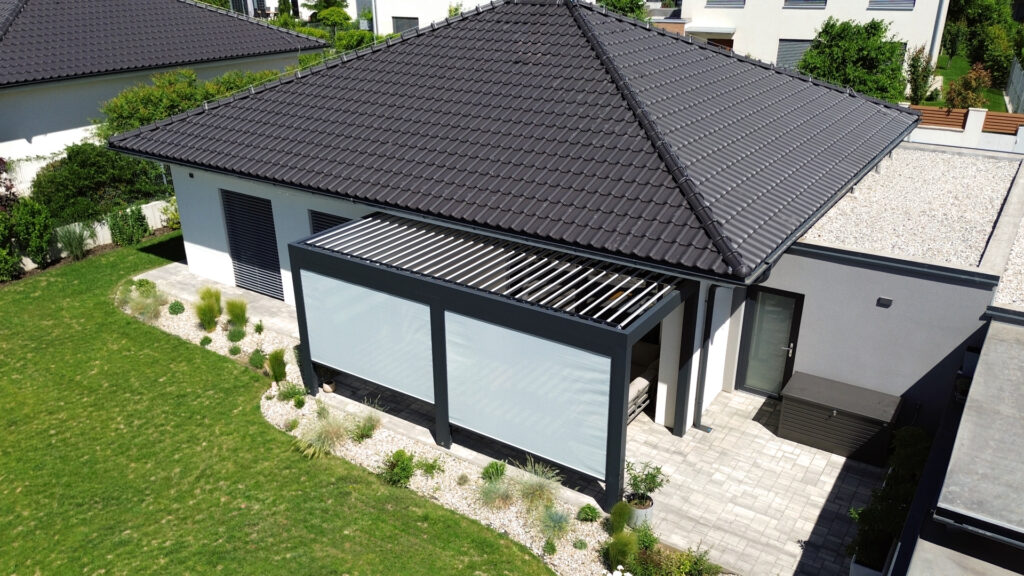 Pergola LAMELINO u rodinného domu se světlými screenovými roletami UNIROL pro boční zastínění terasy.