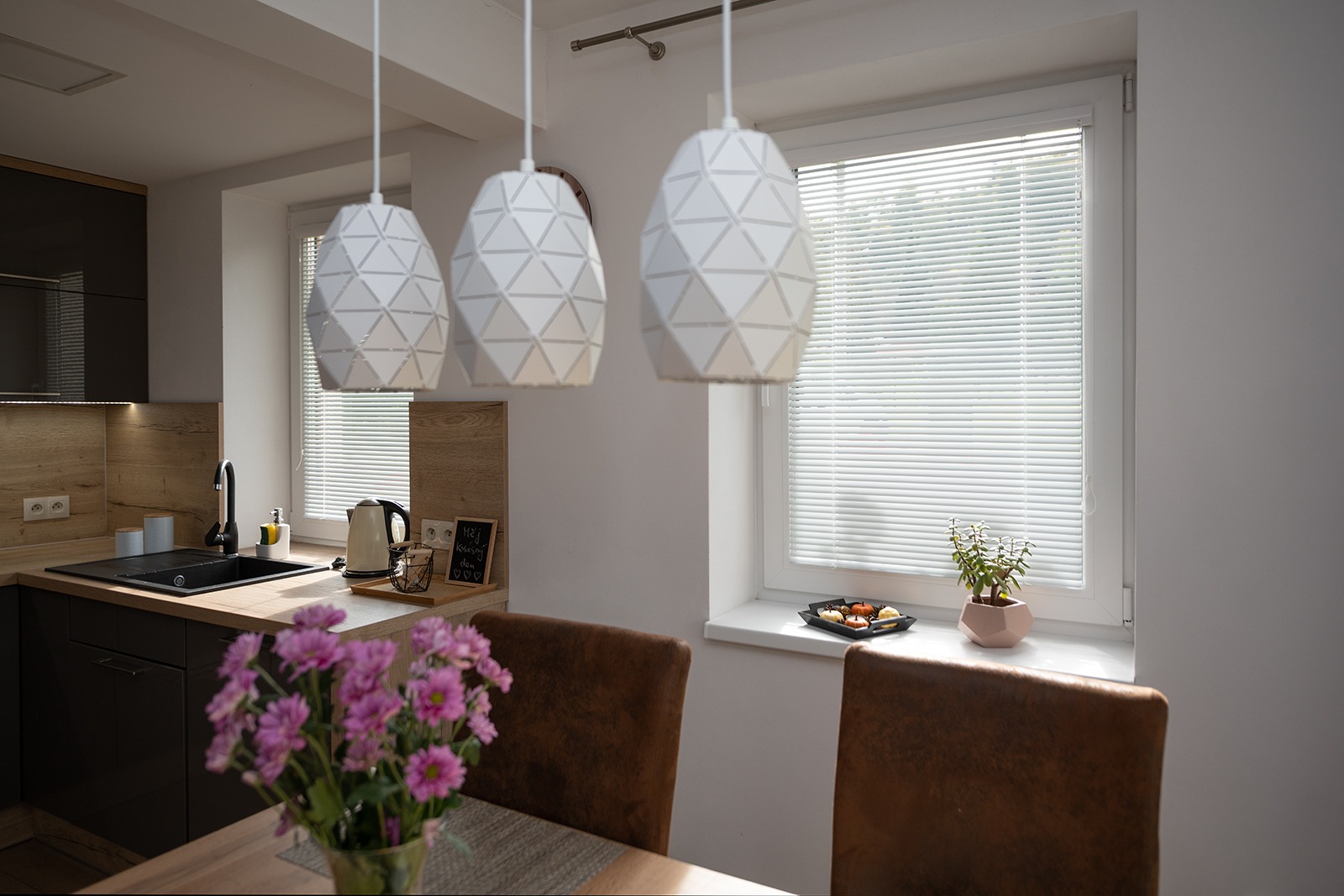 Vnitřní žaluzie na dvou oknech v kuchyni, před nimi stojí stůl