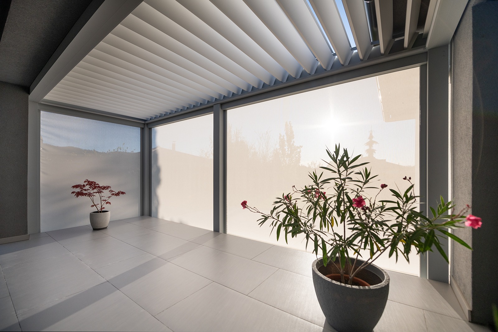 Pergola s pootevřenými lamelami a staženými bočními screenovými clonami na terase